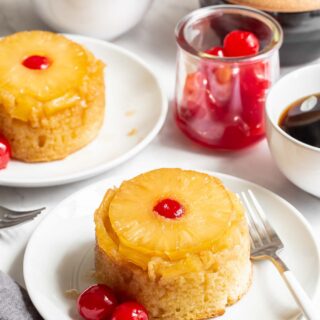 Two mini pineapple upside down cakes on plates.