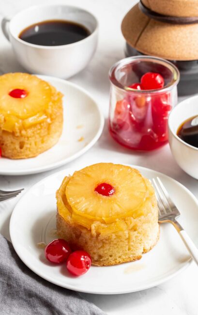 Two mini pineapple upside down cakes on plates.
