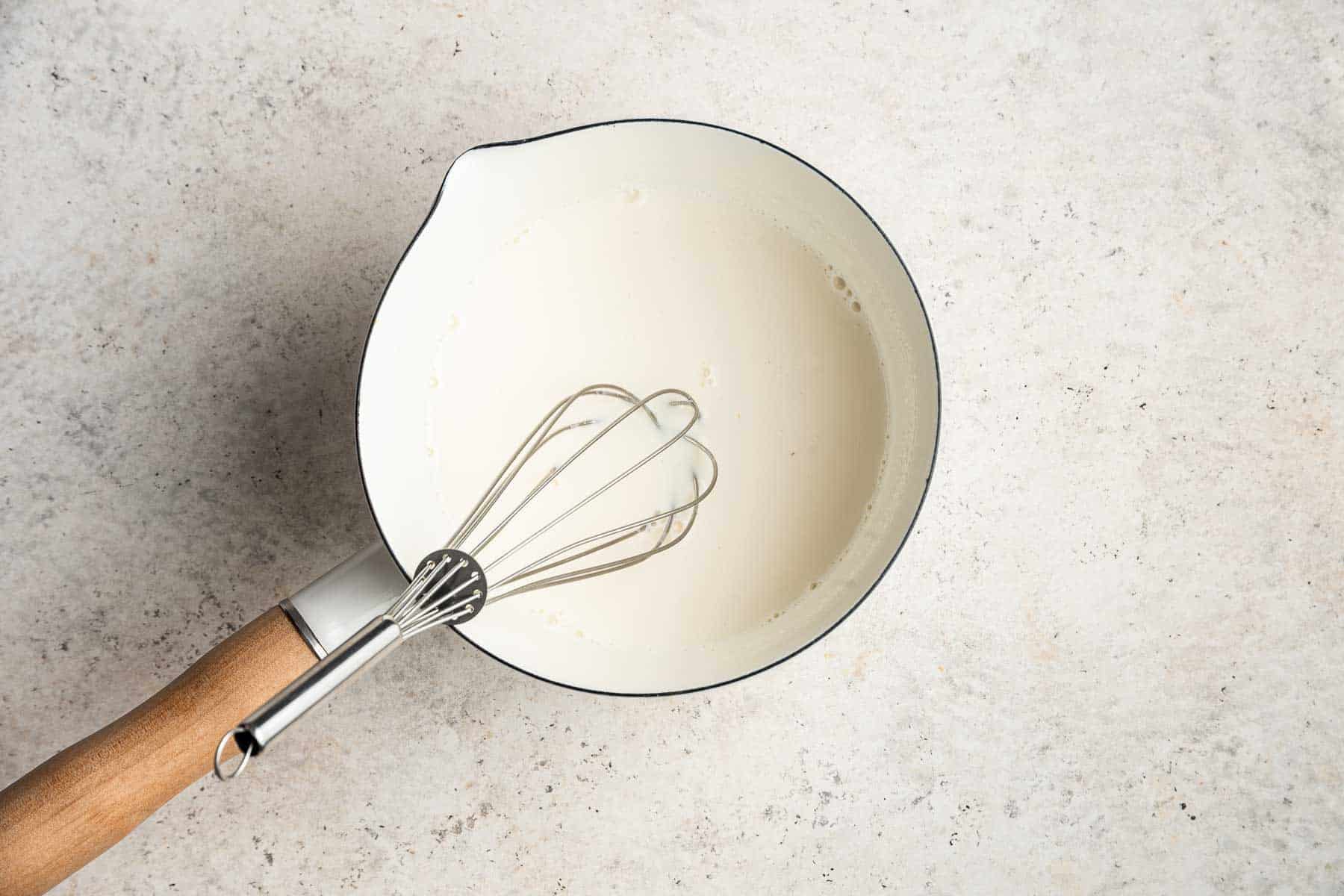 Whisking panna cotta mixture in a white sauce pan.