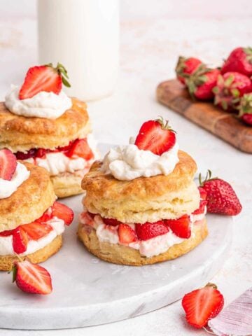Vertical image of 3 strawberry shortcakes on white surface.