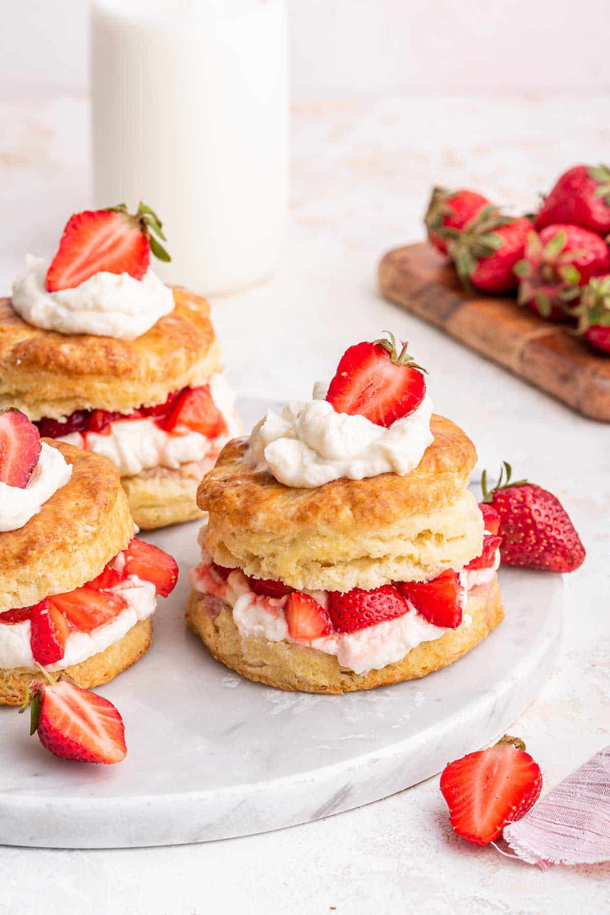 Vertical image of 3 strawberry shortcakes on white surface.