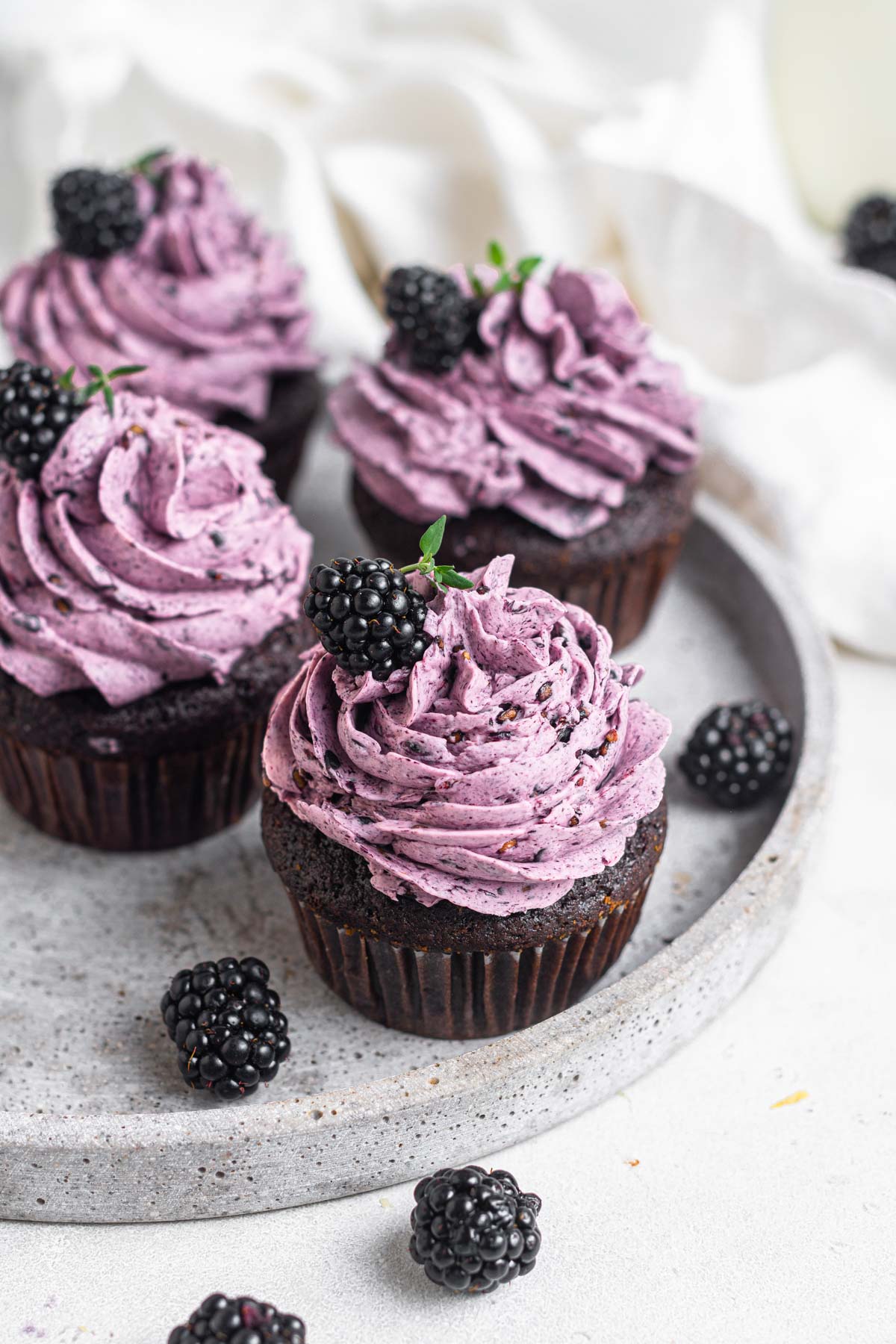 Four chocolate blackberry cupcakes on a white plate.