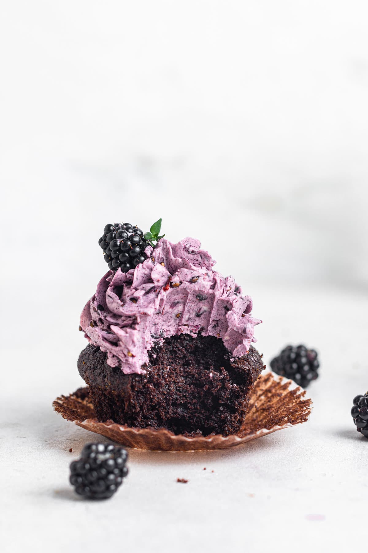 Single chocolate cupcake with blackberry buttercream and a bite missing.