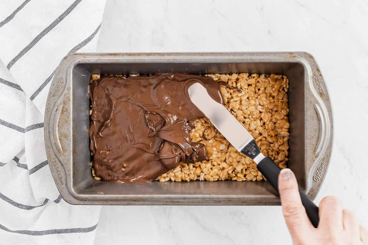 spreading melted chocolate on rice krispies treats in a pan