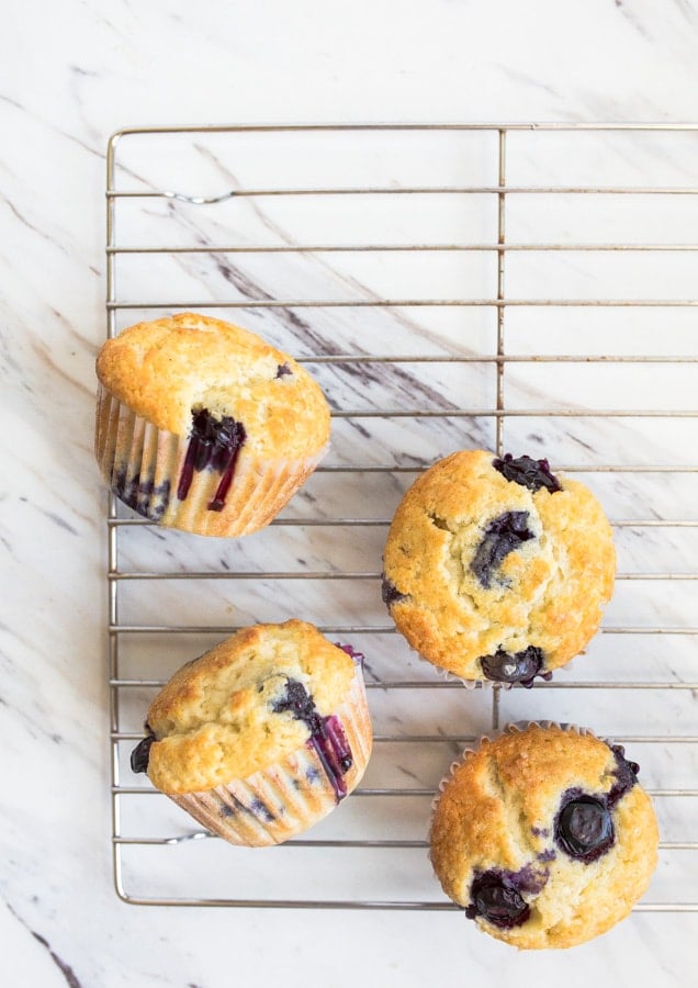 Muffins on a baking rack with fresh burst blueberries.
