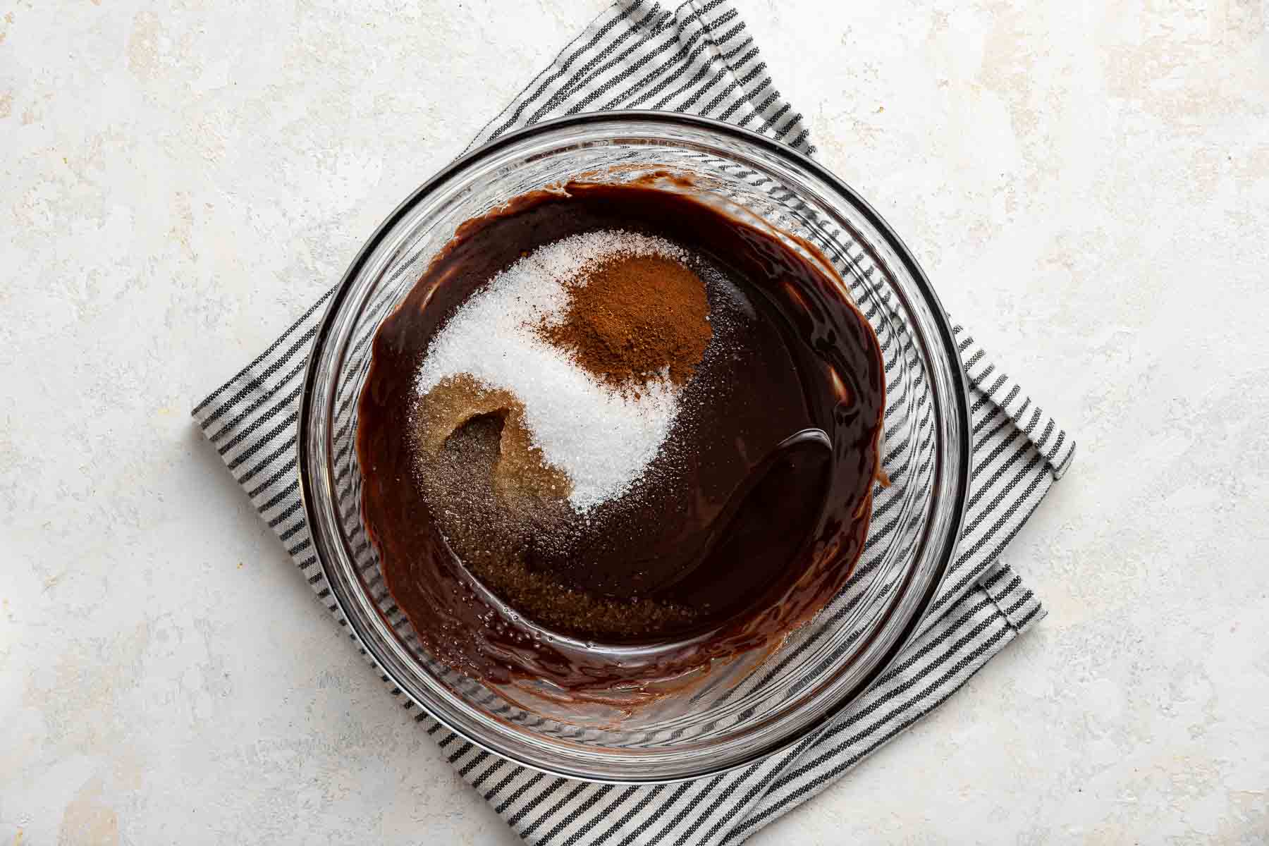 Stirring sugar, espresso powder and vanilla into raw brownie batter in glass bowl.