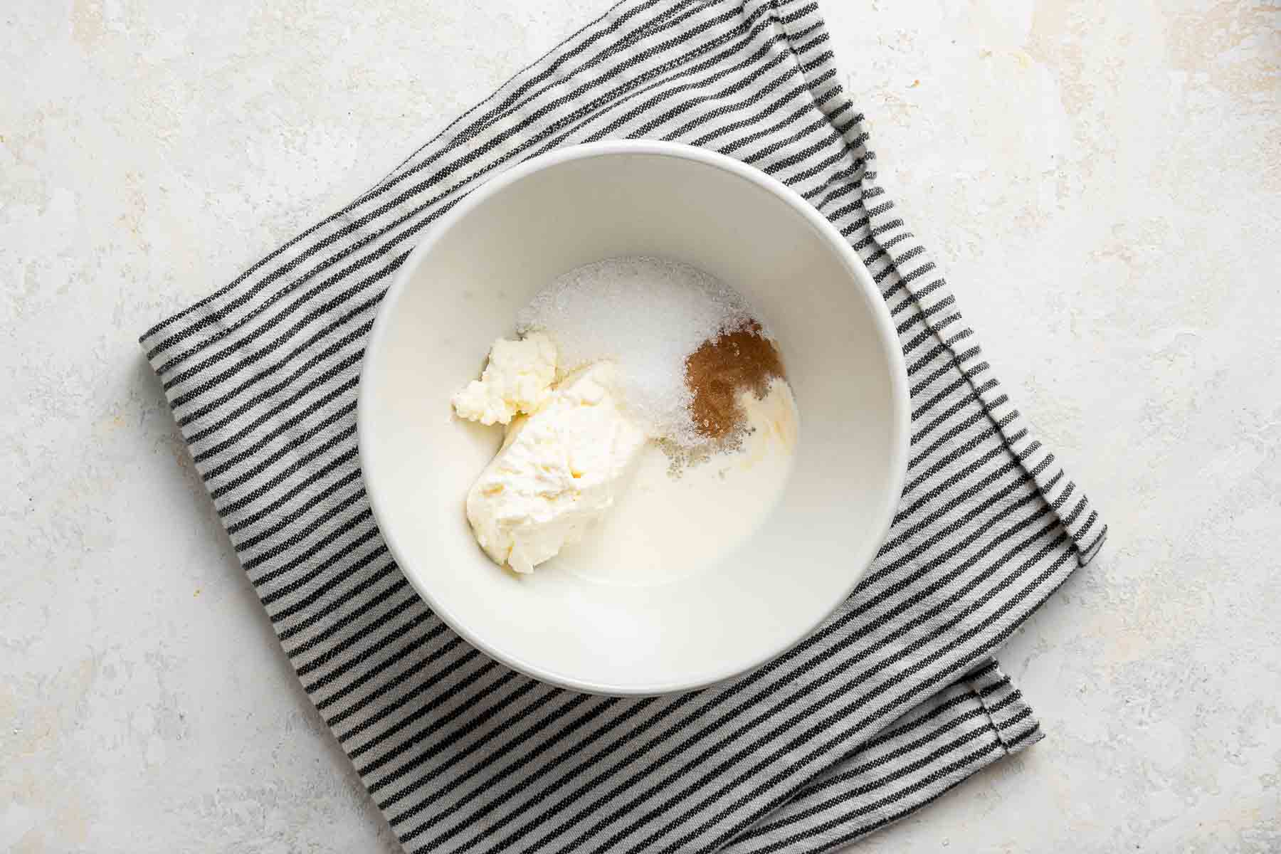 Cream cheese, sugar, vanilla and heavy cream in a white bowl.