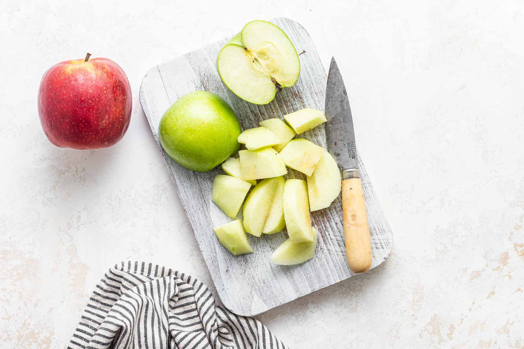 Peeled and sliced apples on cutting board with knife.