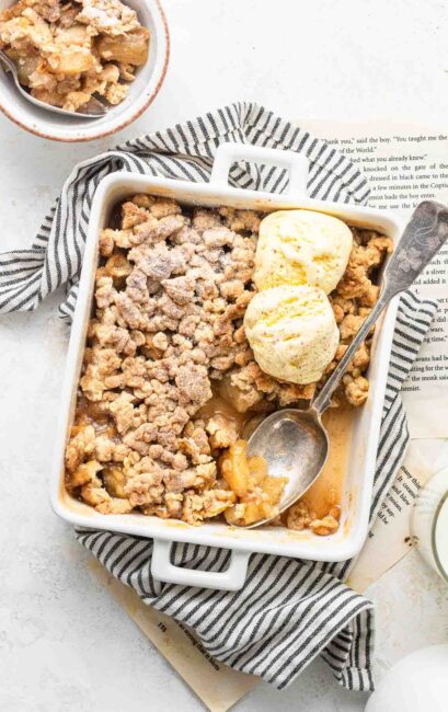 Apple crisp for two in a small baking dish with two scoops of ice cream.