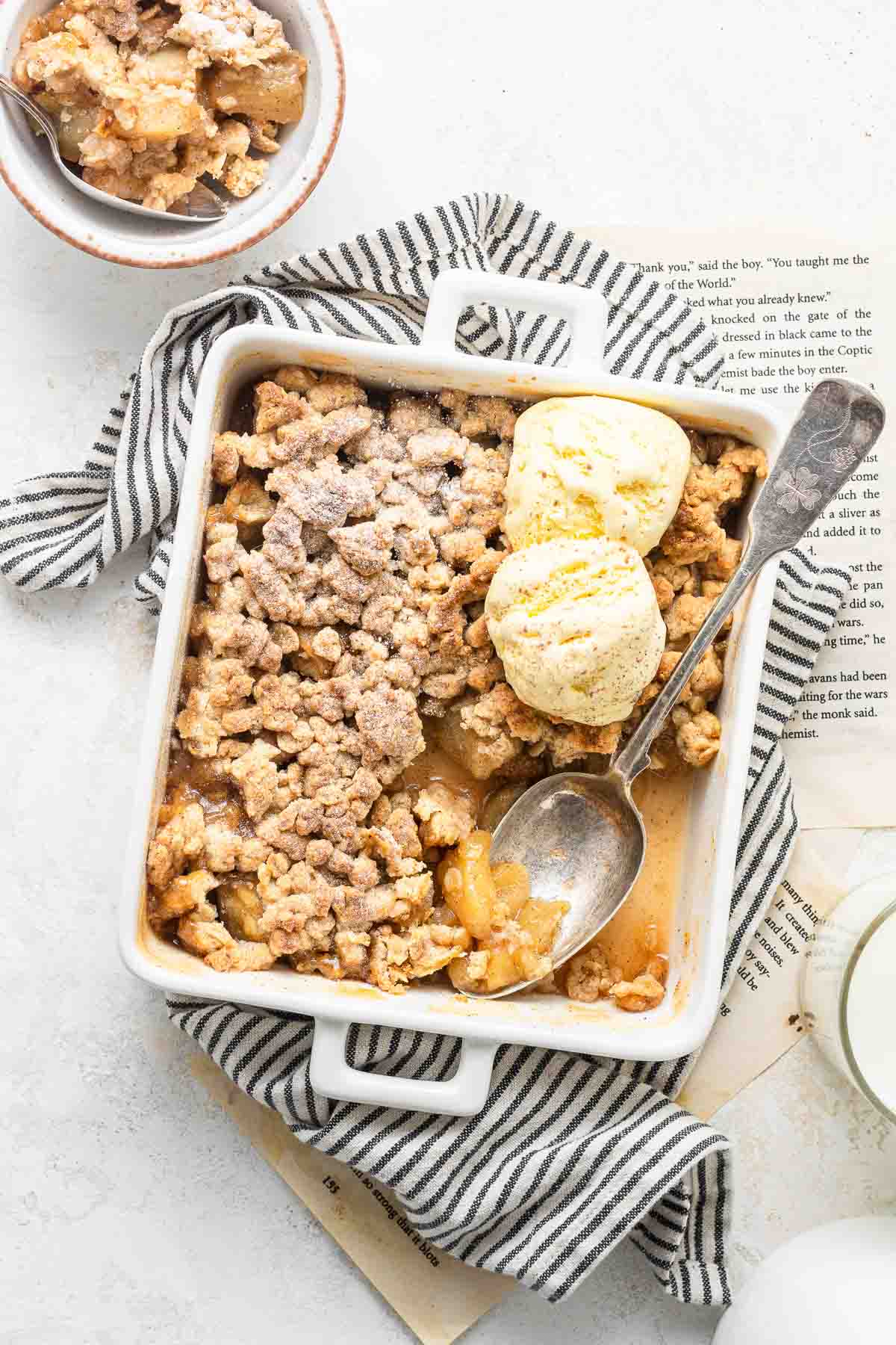 Apple crisp for two in a small baking dish with two scoops of ice cream.
