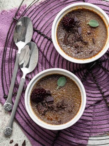Two ramekins of chocolate creme brulee on wire rack with spoons.