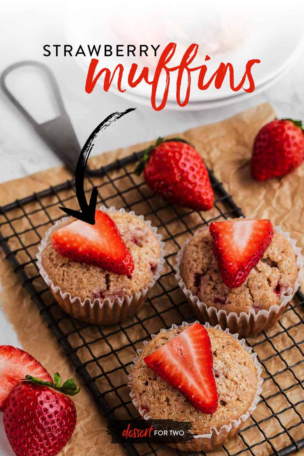 Three strawberry muffins on a wire rack with fresh berries on top.