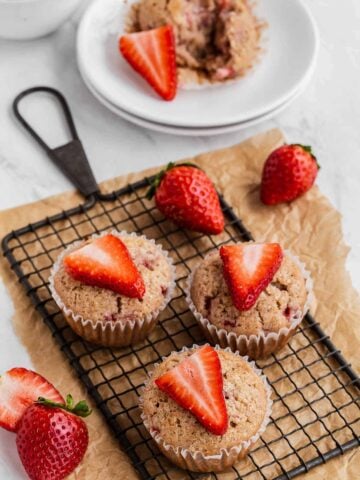 Strawberry Muffins on a wire rack with fresh strawberry slices on top.