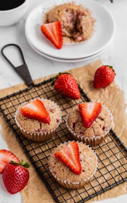 Strawberry Muffins on a wire rack with fresh strawberry slices on top.
