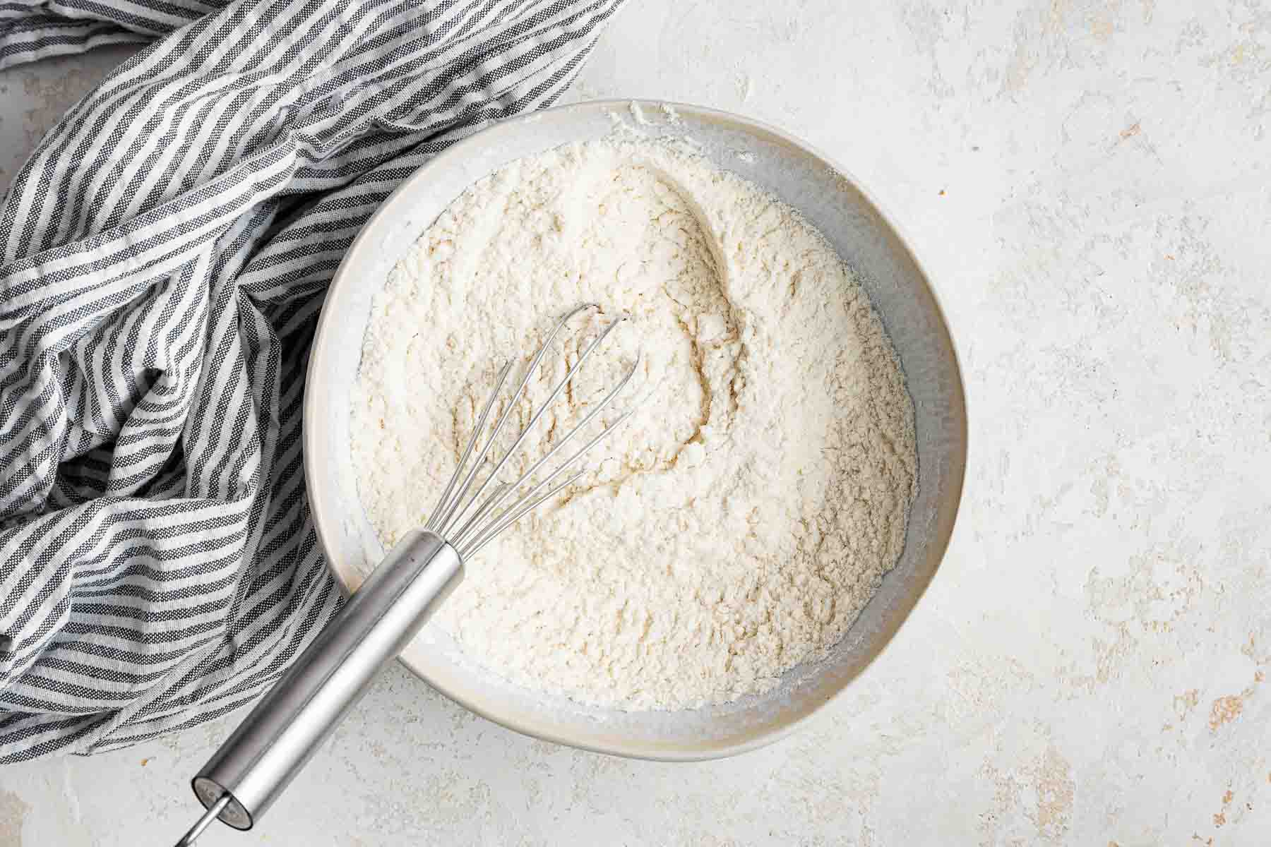 White bowl with flour and baking soda being whisked together.