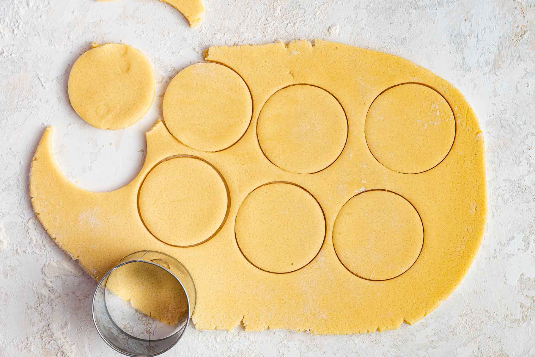 Yellow dough rolled out with numerous circle cookie cut outs missing.