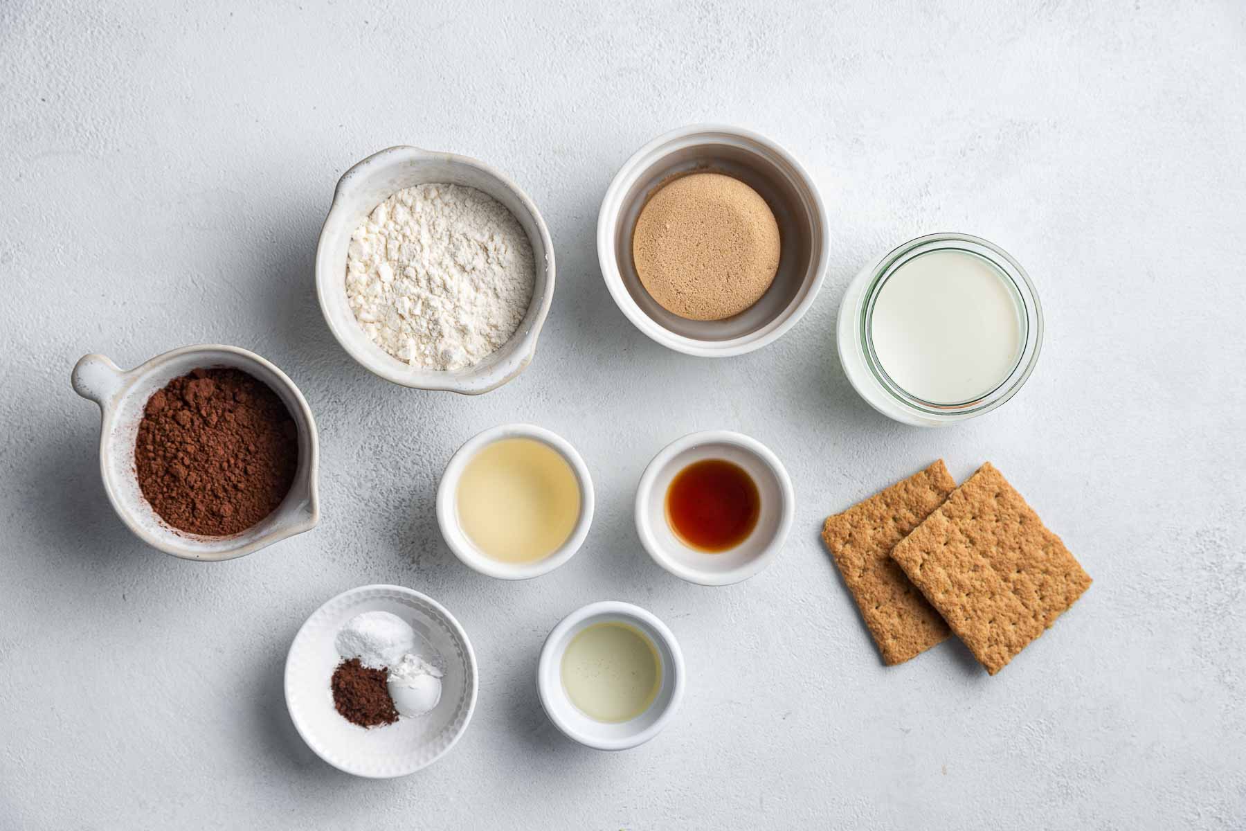Ingredients for chocolate graham cracker cupcakes in small bowls on table.