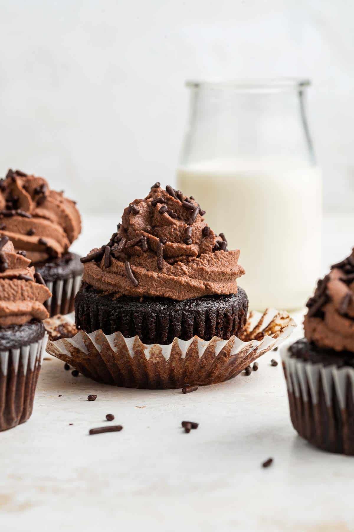 Four chocolate cupcakes in front of a glass of milk.