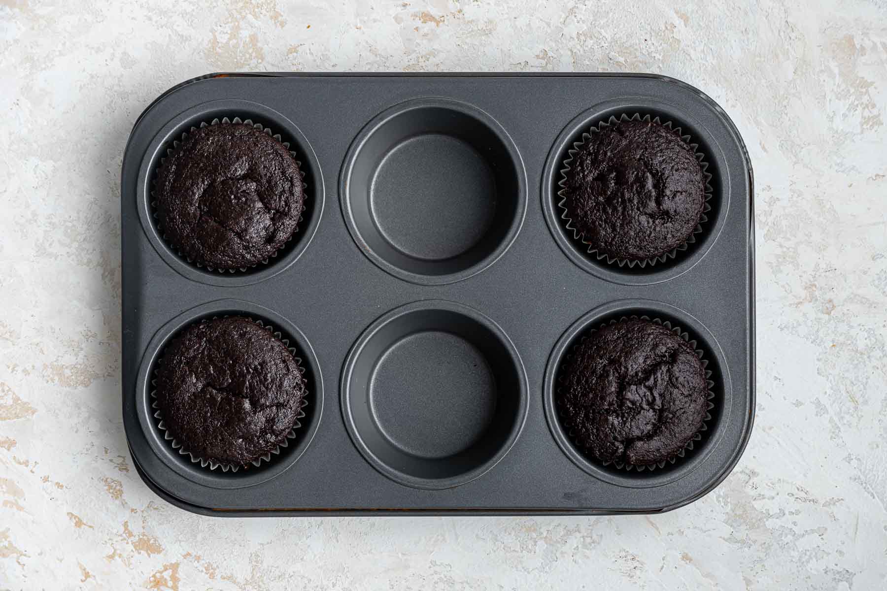 Four freshly baked chocolate cupcakes in a muffin pan.