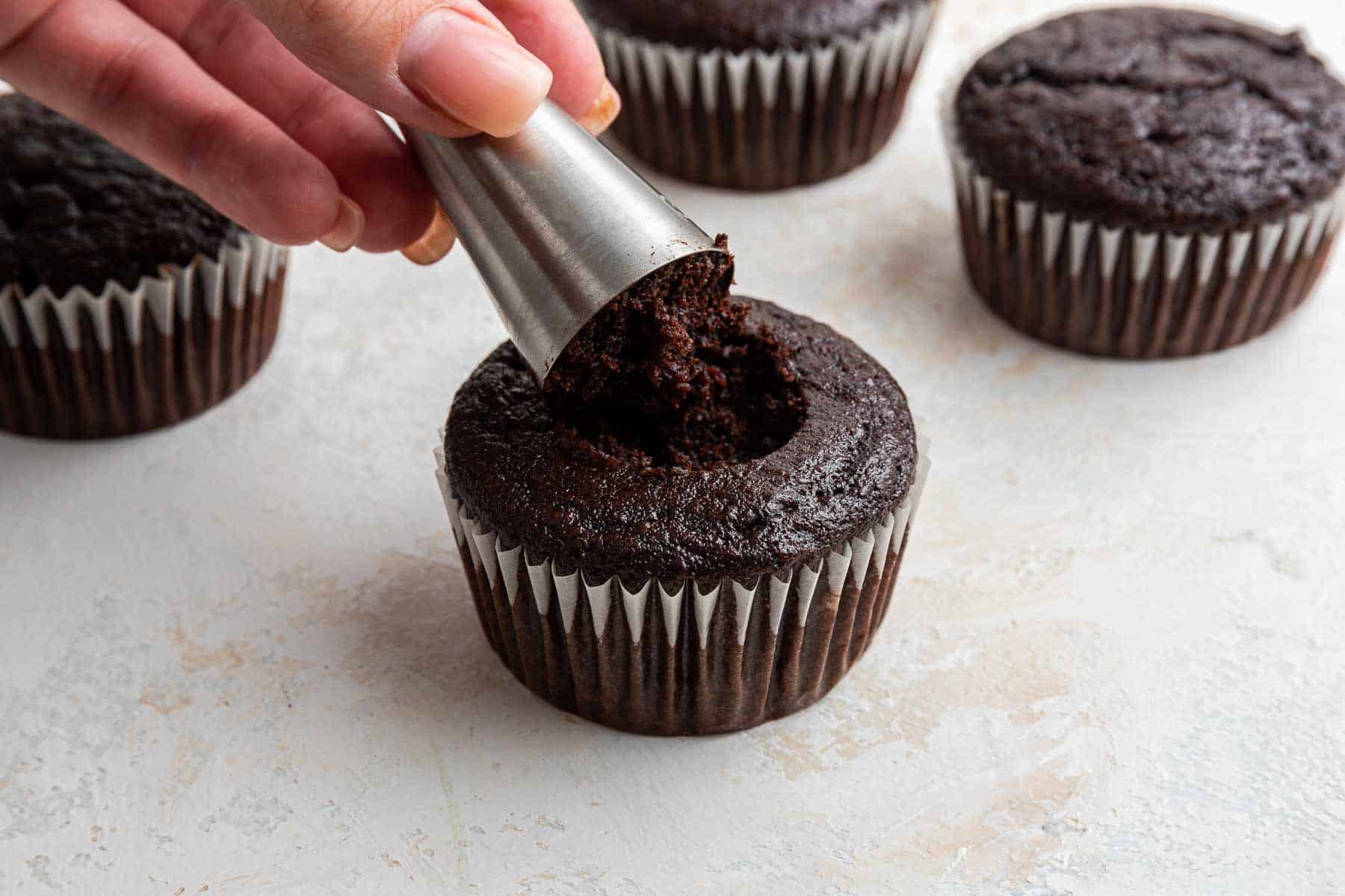 Using a piping tip to make a well in the center of a chocolate cupcake.