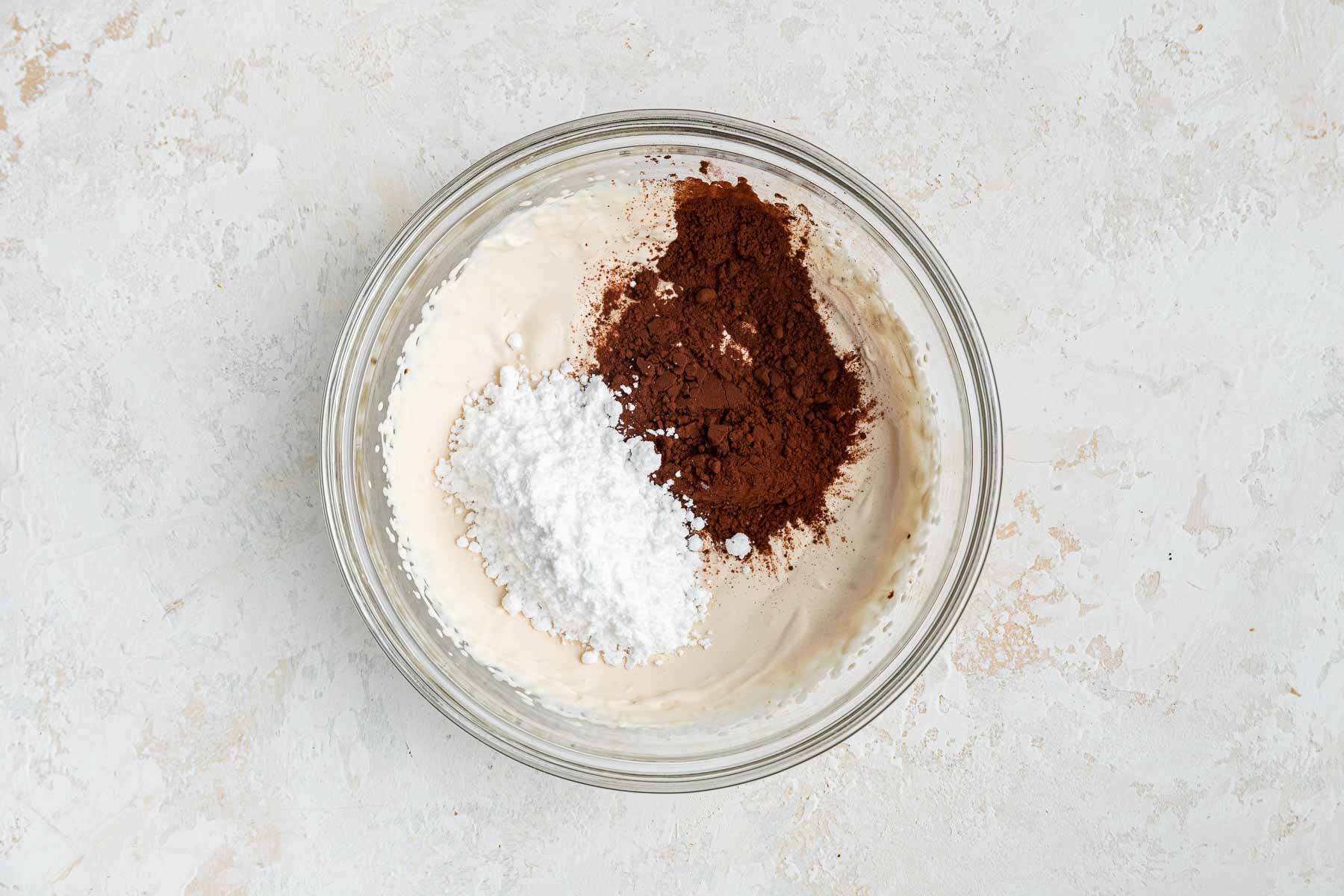 Heavy whipping cream in bowl with powdered sugar and cocoa powder on top.