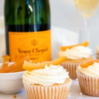 White cupcakes with champagne bottle in background.