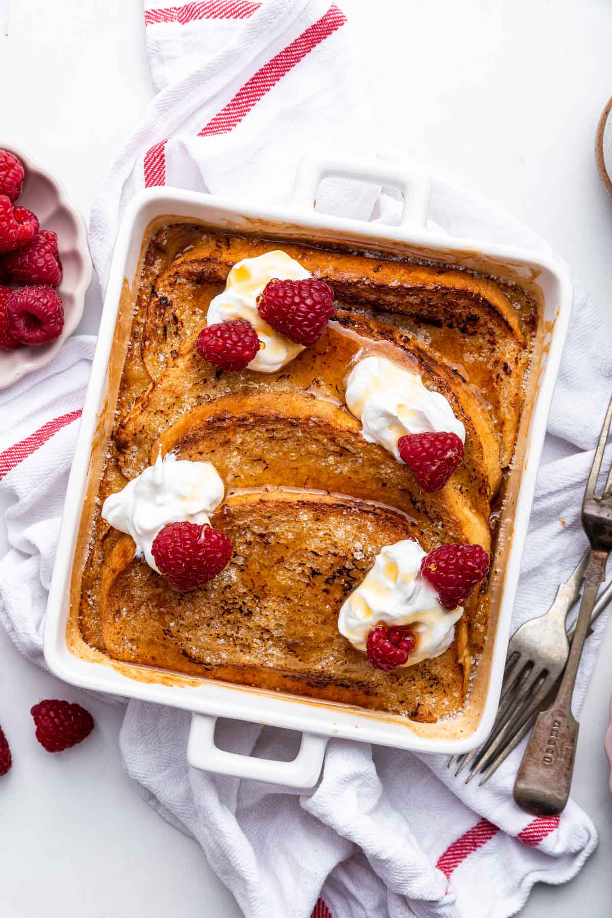 Vertical image of creme brulee French toast garnished with raspberries and whipped cream.