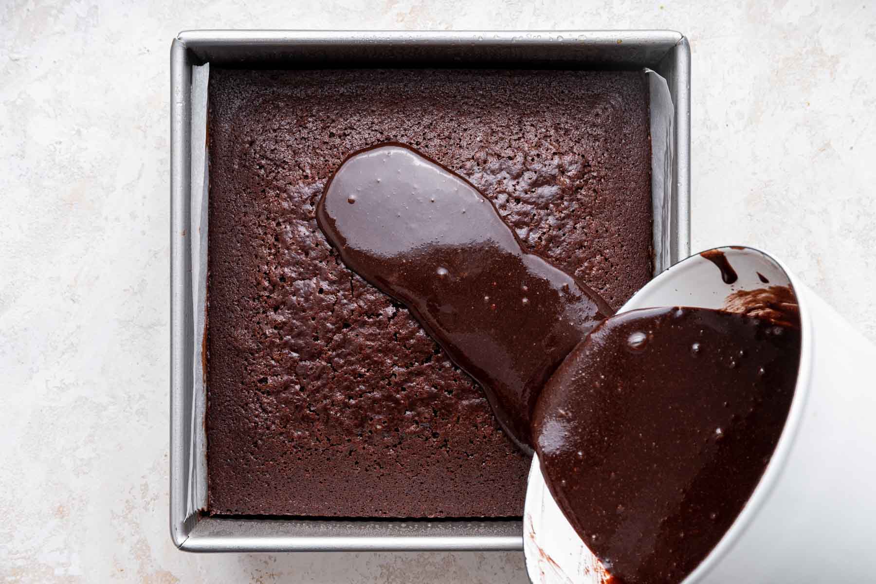 Pouring warm melted chocolate icing on a square Dr Pepper chocolate cake.