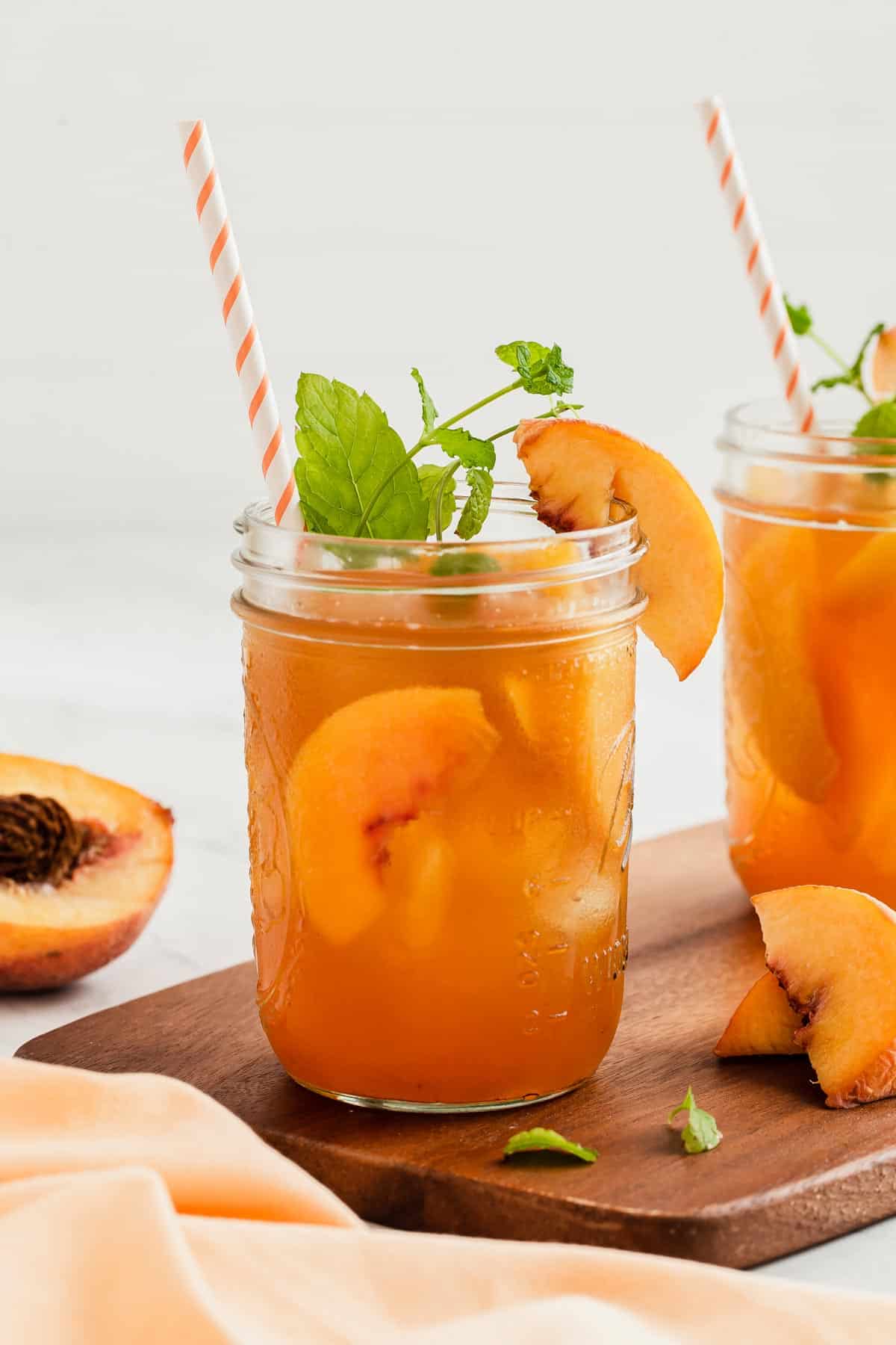 Two jars of iced tea with fresh peaches and mint sprigs.