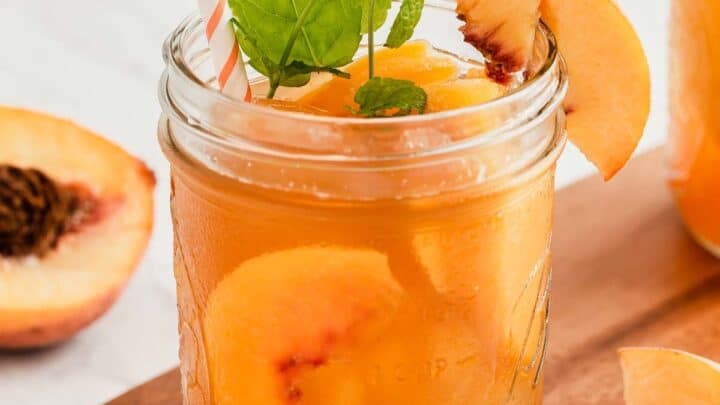 Mason jar of peach iced tea with fresh mint sprig.
