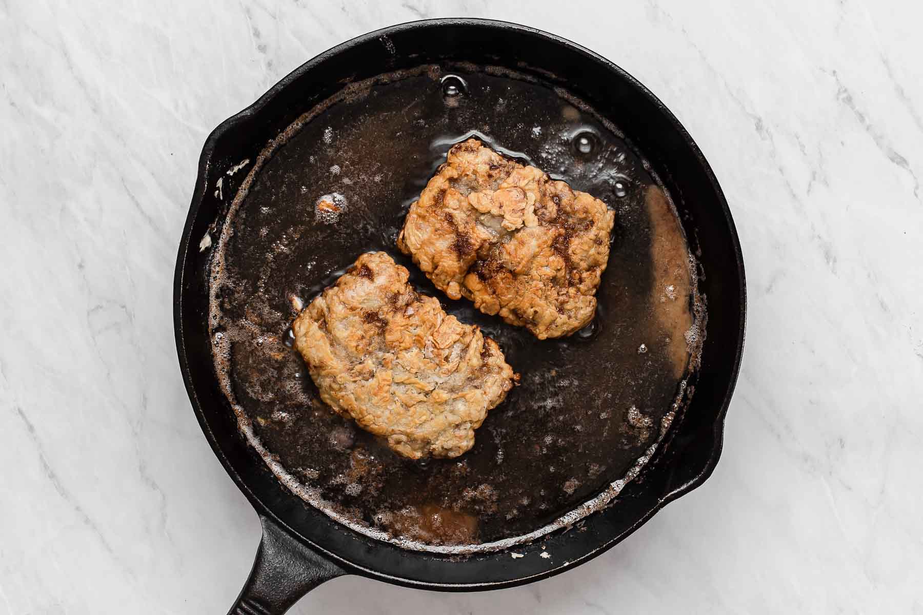 Chicken fried steak in cast iron skillet.