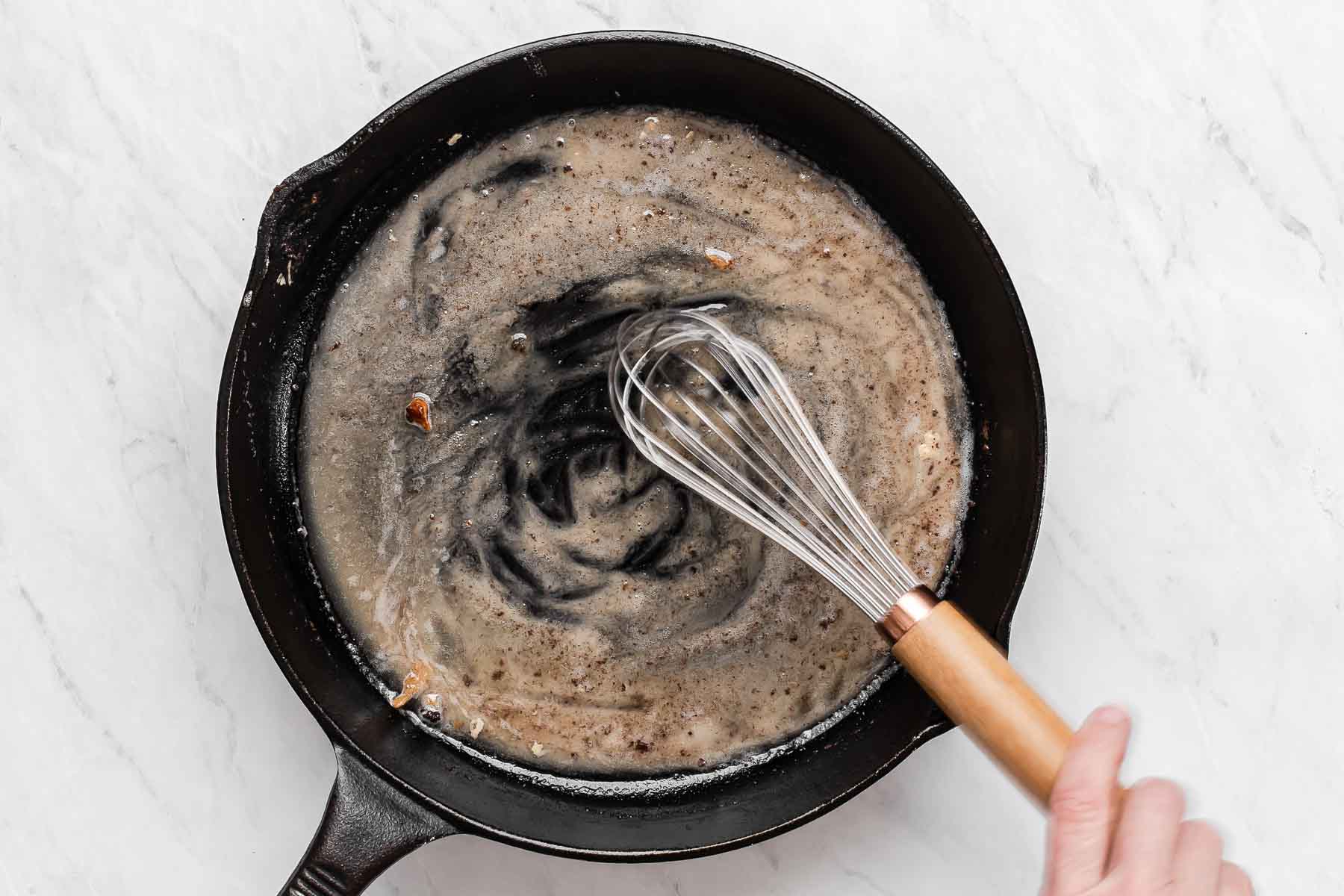 Making gravy in a cast iron skillet with whisk.