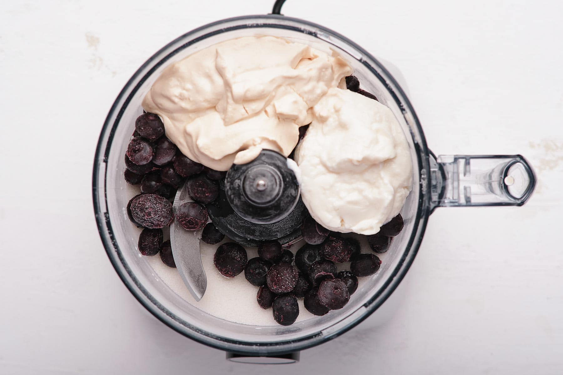 Blueberries, yogurt, and heavy cream in a food processor bowl.