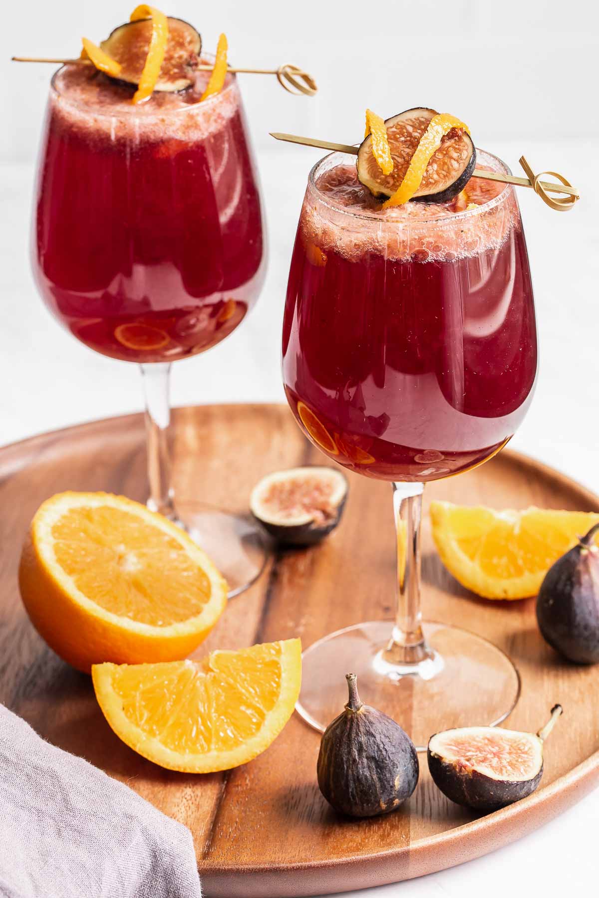 Two red wine sangria wine glasses on plate with oranges.