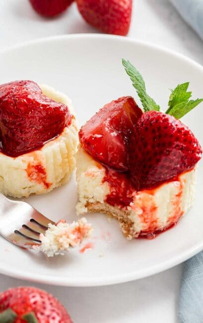 Two mini strawberry cheesecakes on a plate with a fork.