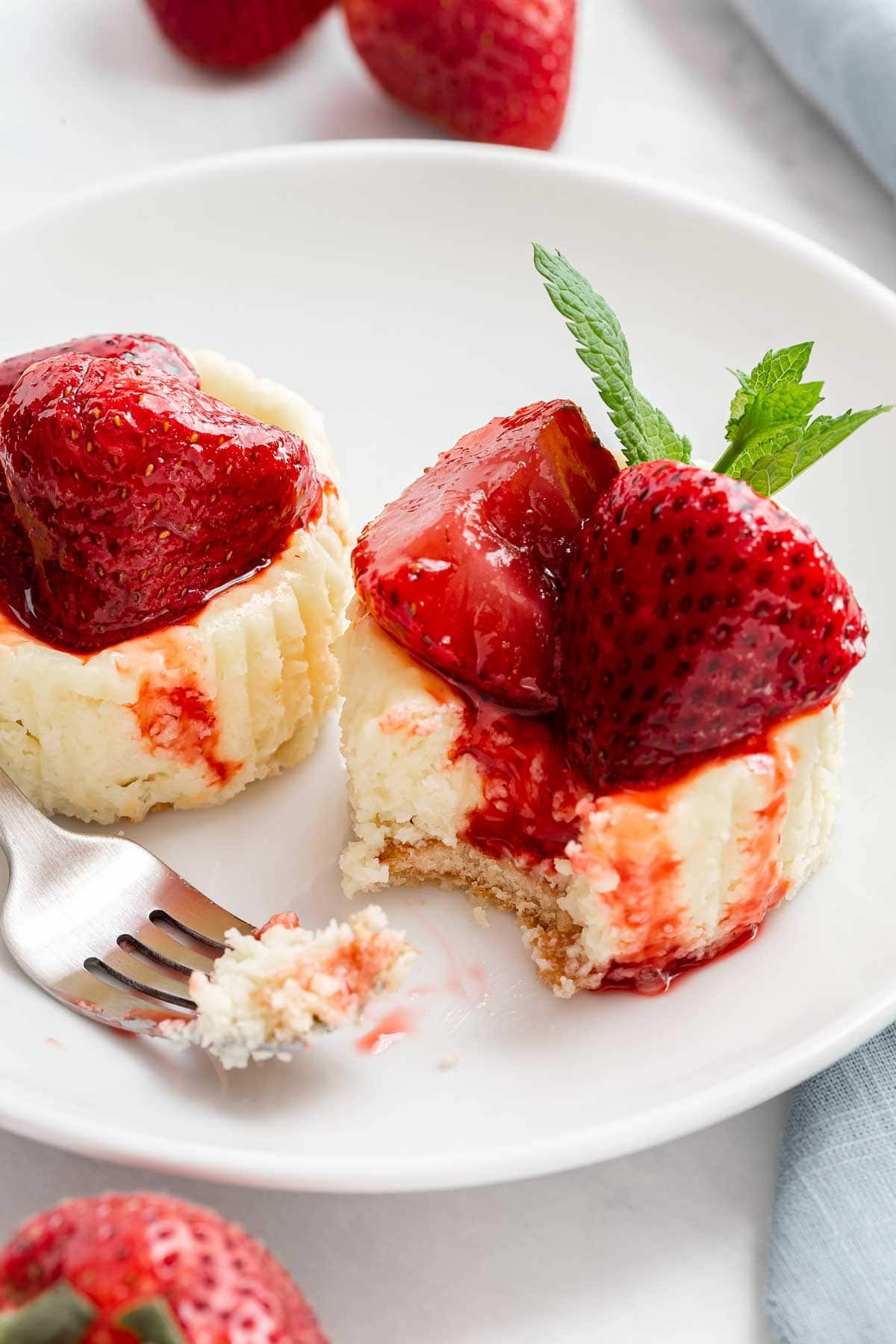 Two mini strawberry cheesecakes on a plate with a fork.