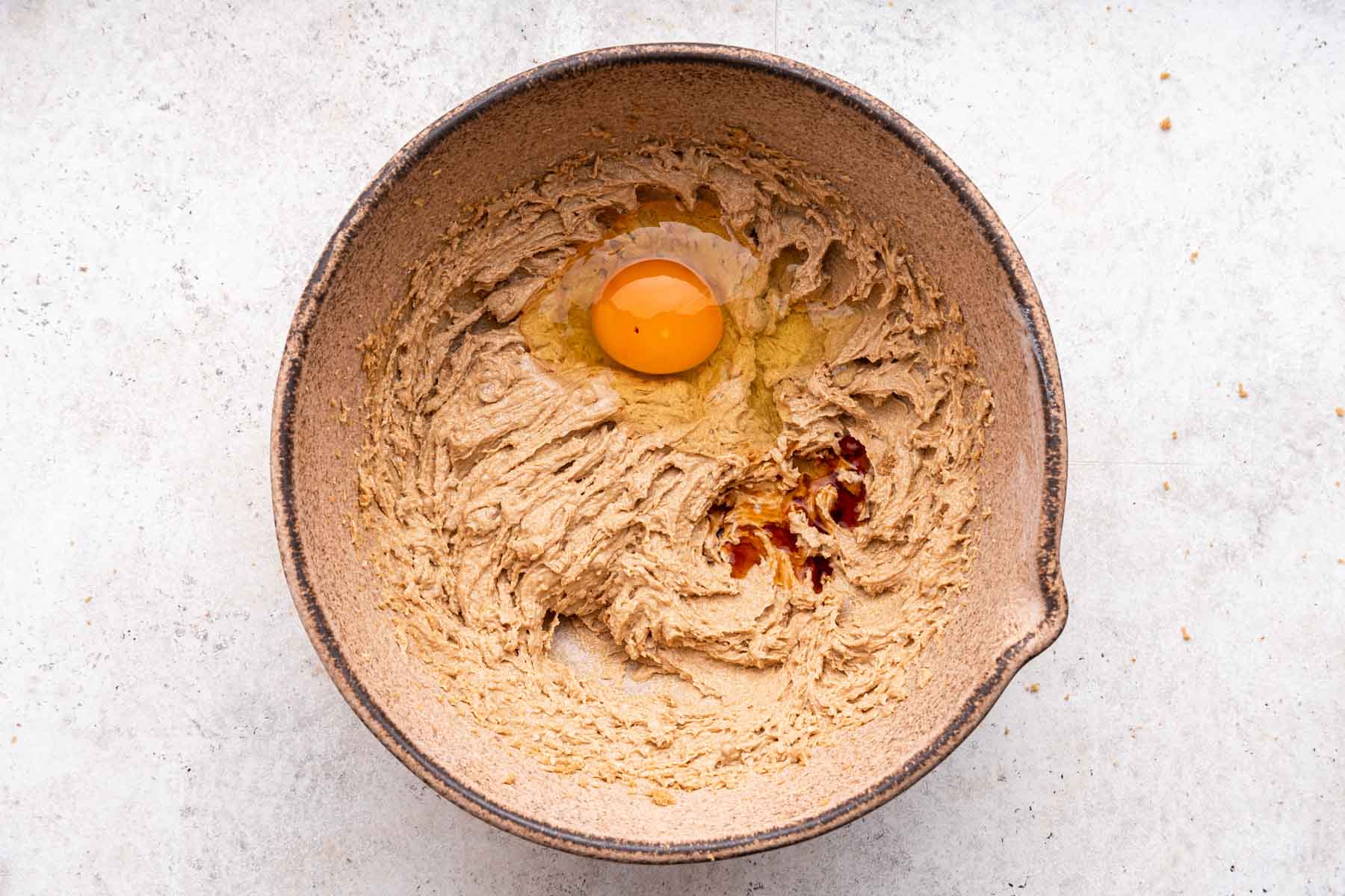 Egg yolk and vanilla in brown dough in a brown mixing bowl.