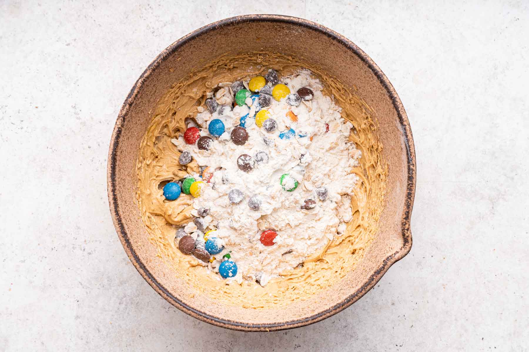 Flour and colorful chocolate candies over dough in mixing bowl.