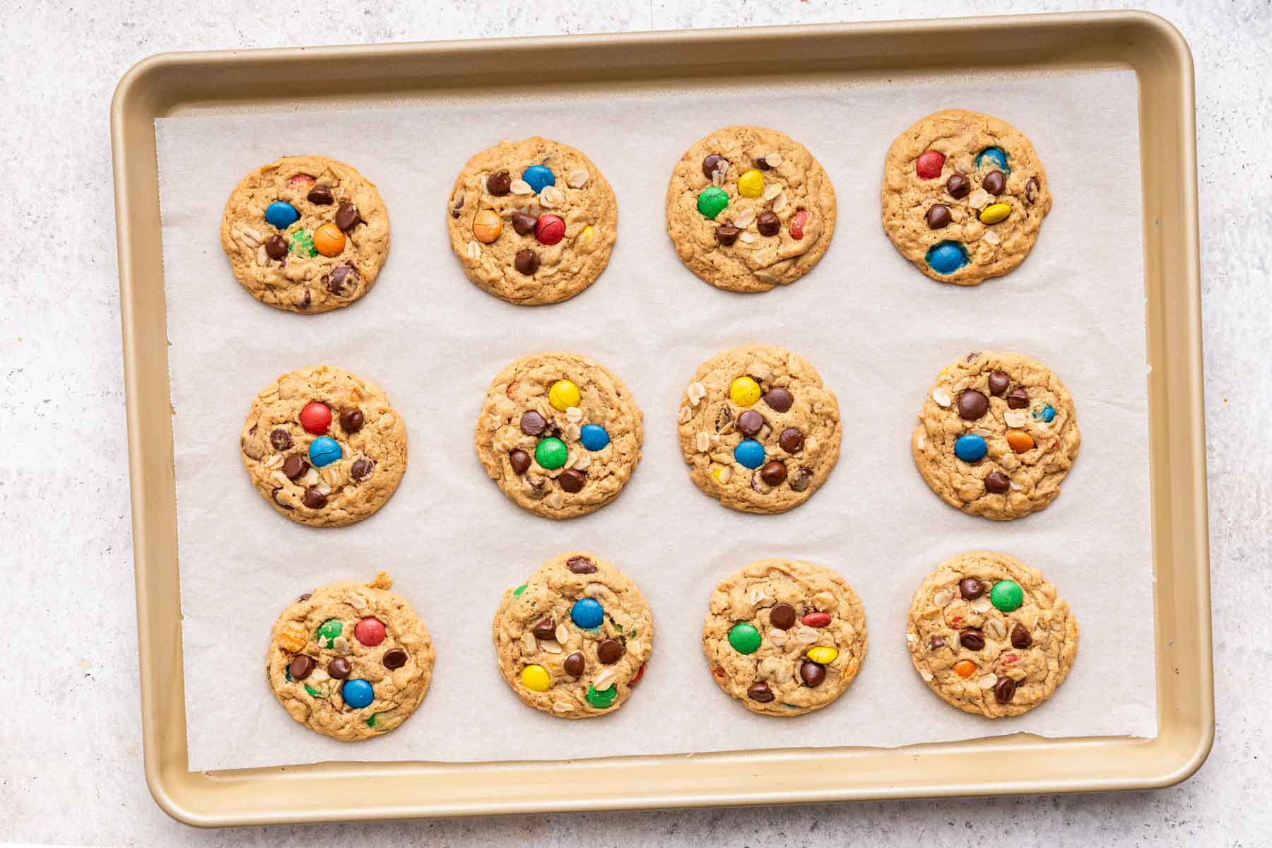Twelve monster cookies baked on a gold sheet pan.