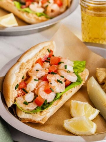 Fresh shrimp po boy sandwiches served with lemon wedges and a pickle.