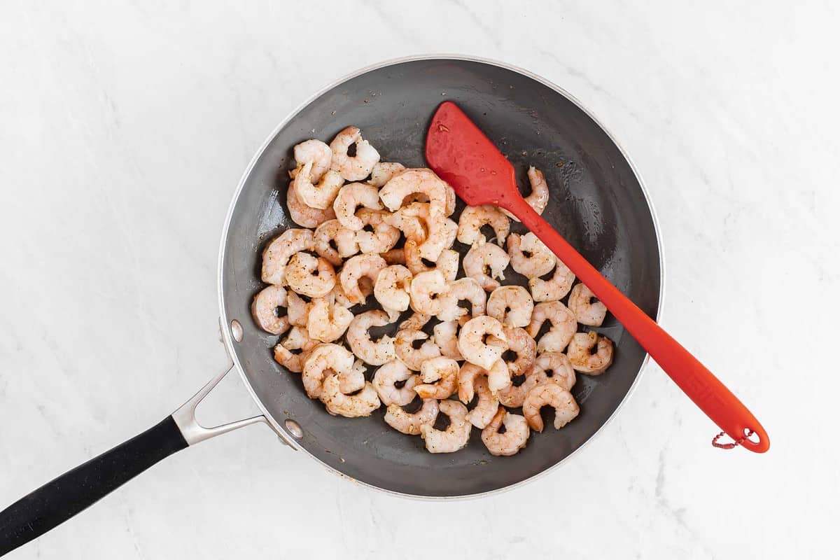 Sautéed shrimp in a skillet with red spatula.