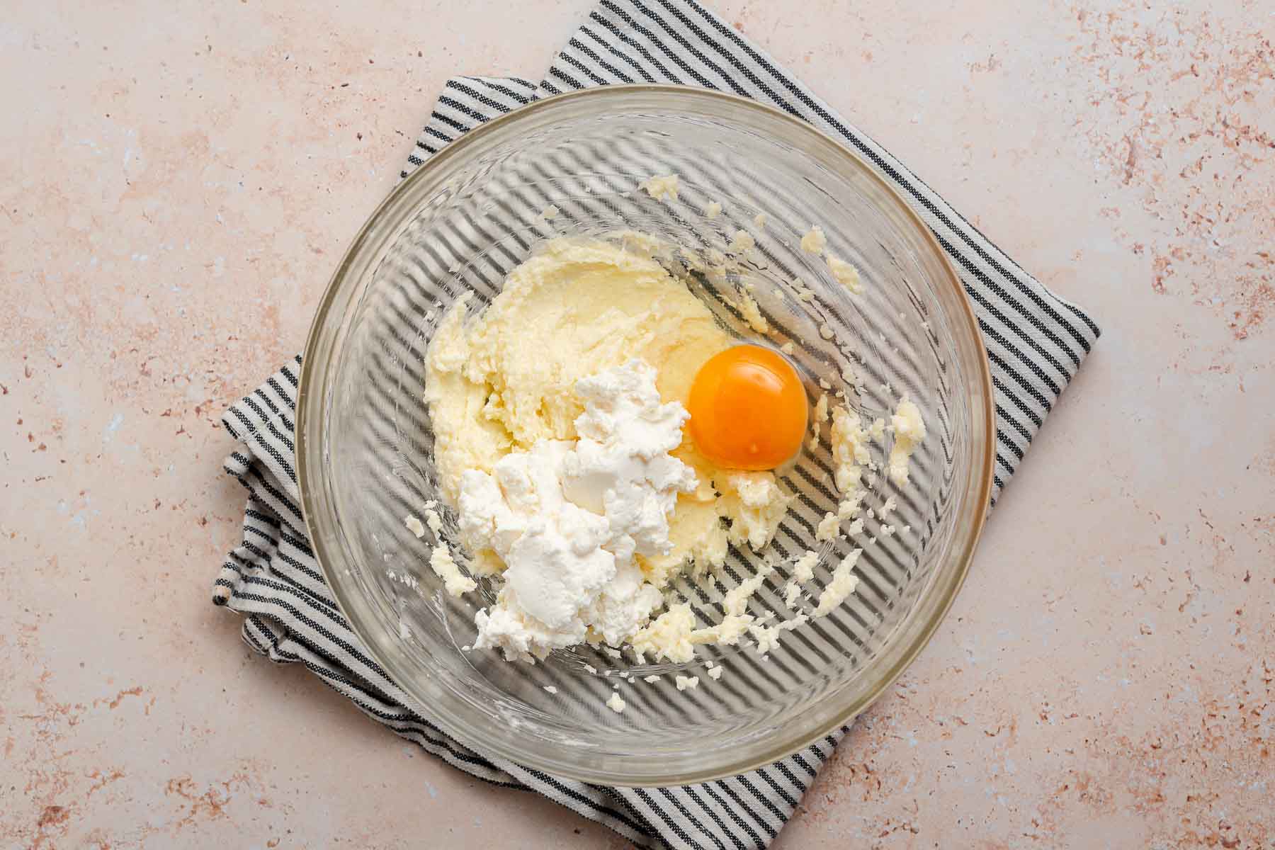 Egg and ricotta added to cake batter in glass bowl.