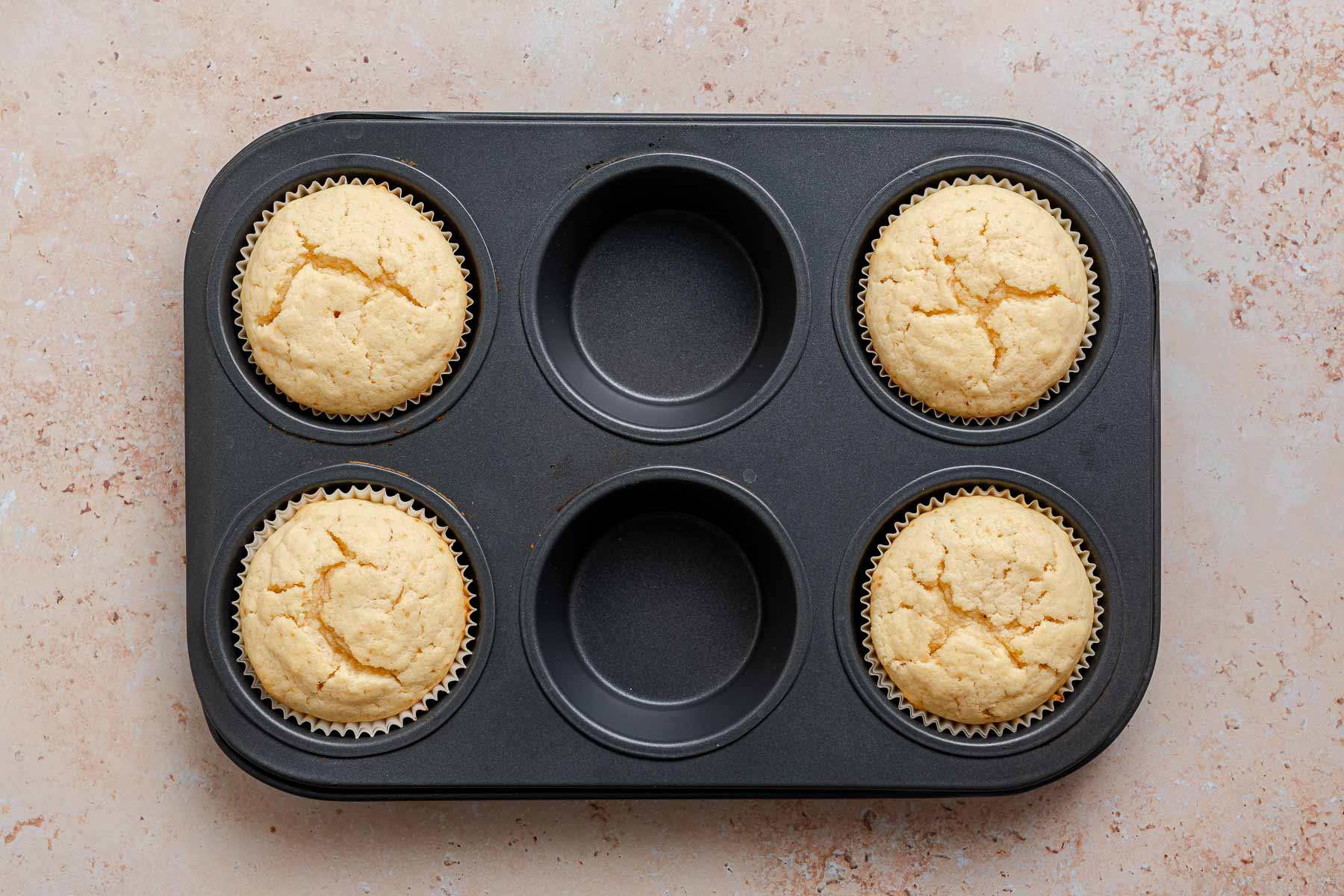 Four baked cupcakes in a muffin pan.