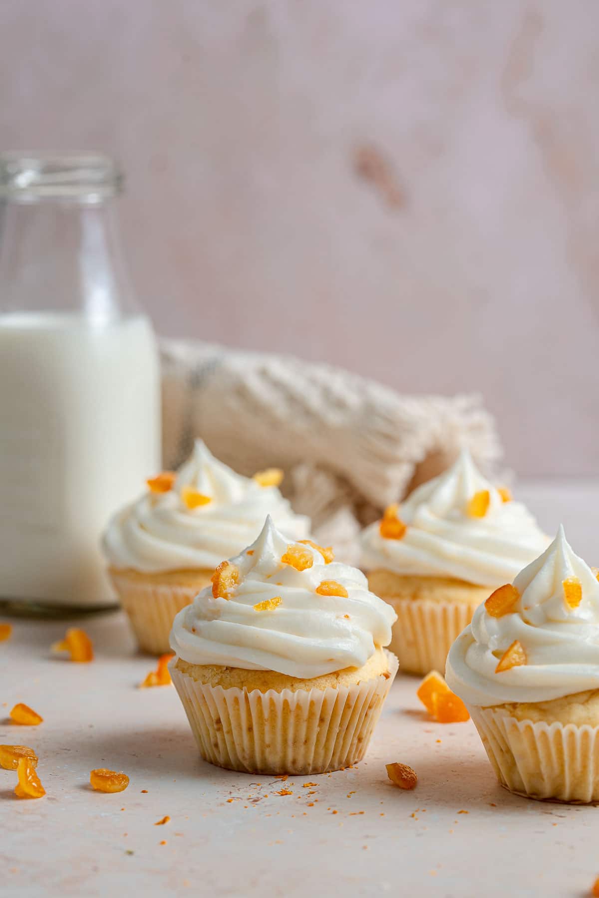 Four white cupcakes with white frosting on table.