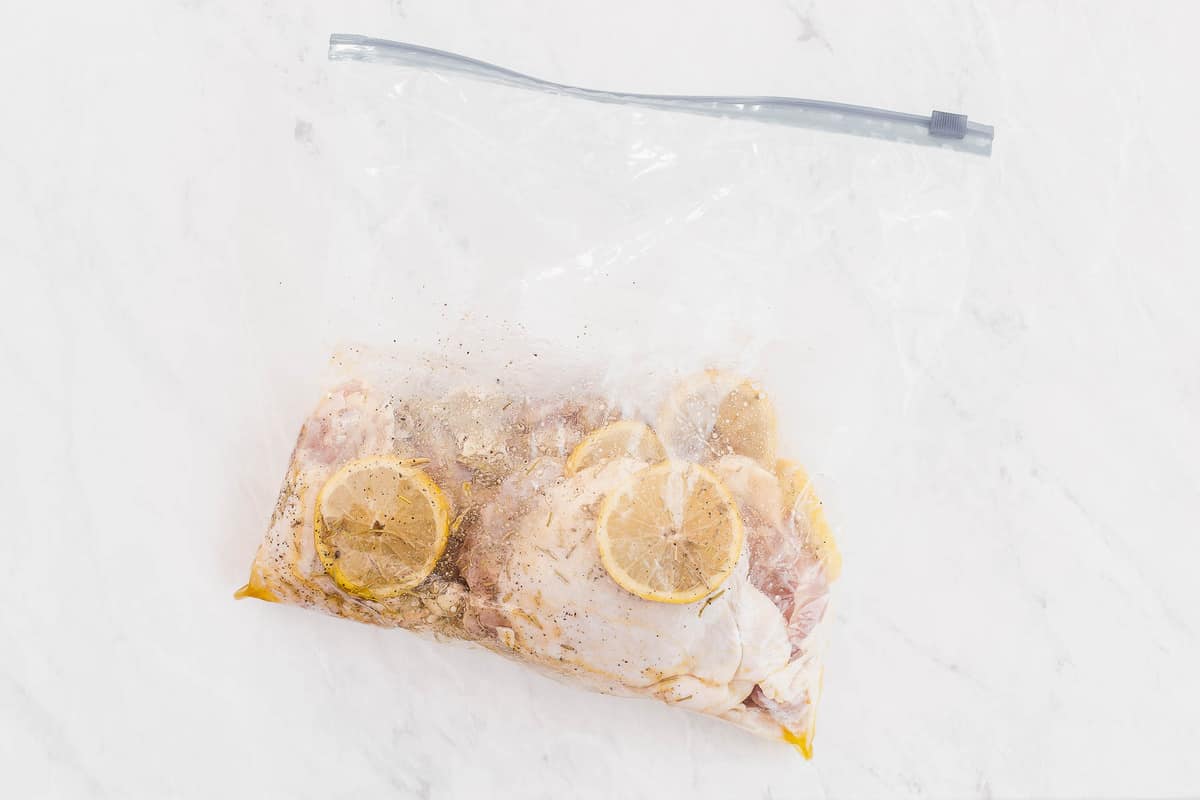 chicken thighs in a plastic bag with lemon slices and rosemary