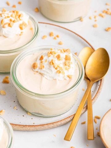 Four glass jars of peanut butter mousse decorated with crushed peanuts and gold spoons.