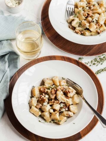 Two serving plates of ricotta gnocchi with white wine on the side.