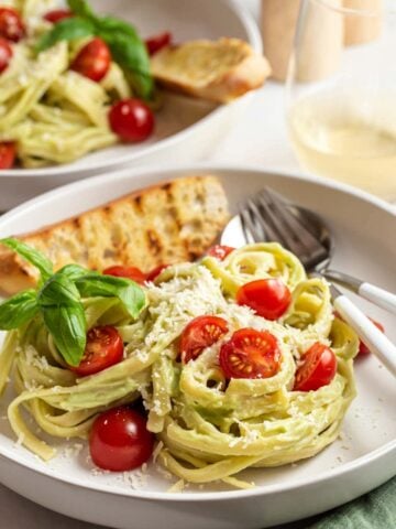 Avocado pasta with tomatoes and grilled bread on plates.