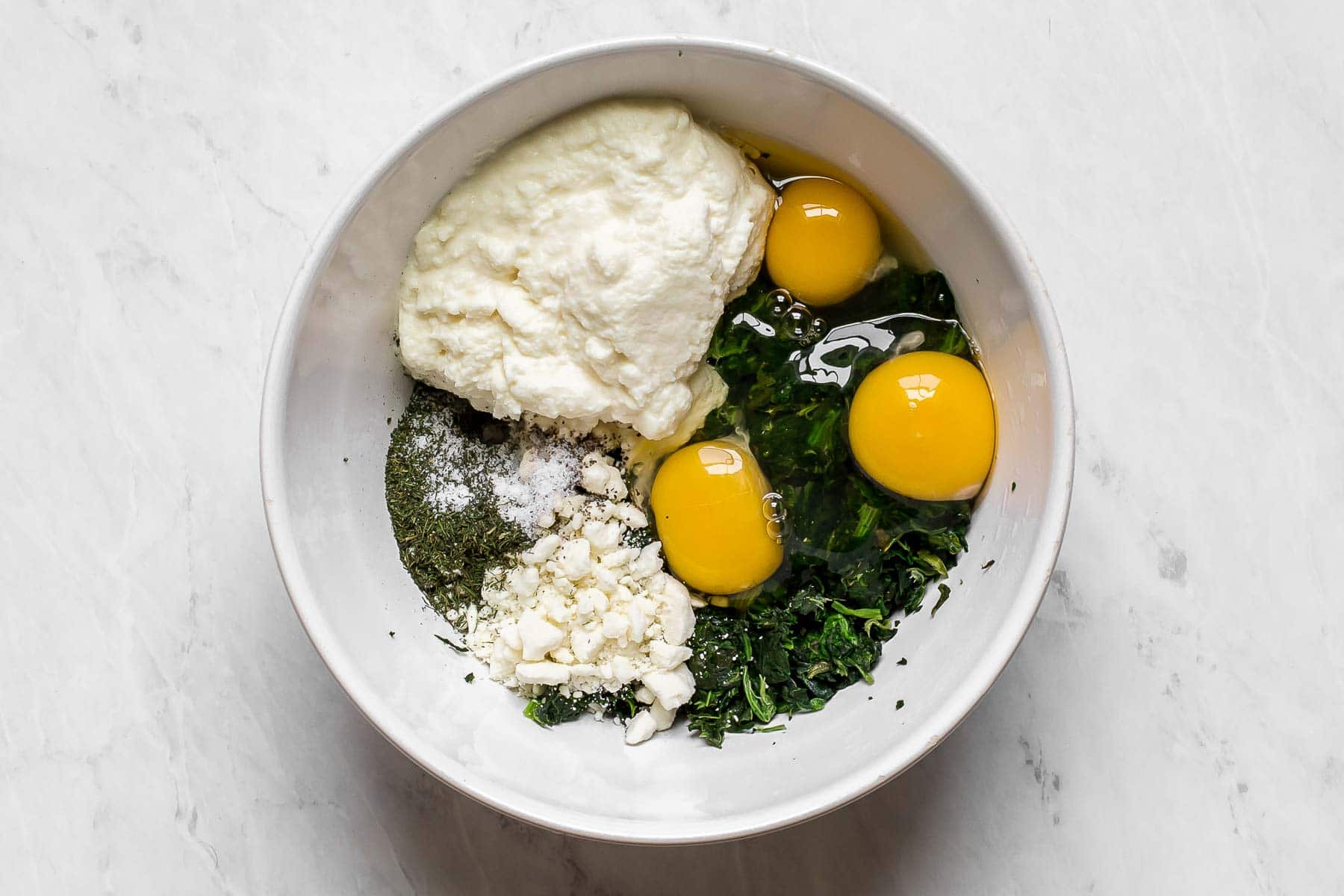 Spinach, ricotta, eggs, and feta in a large white bowl.