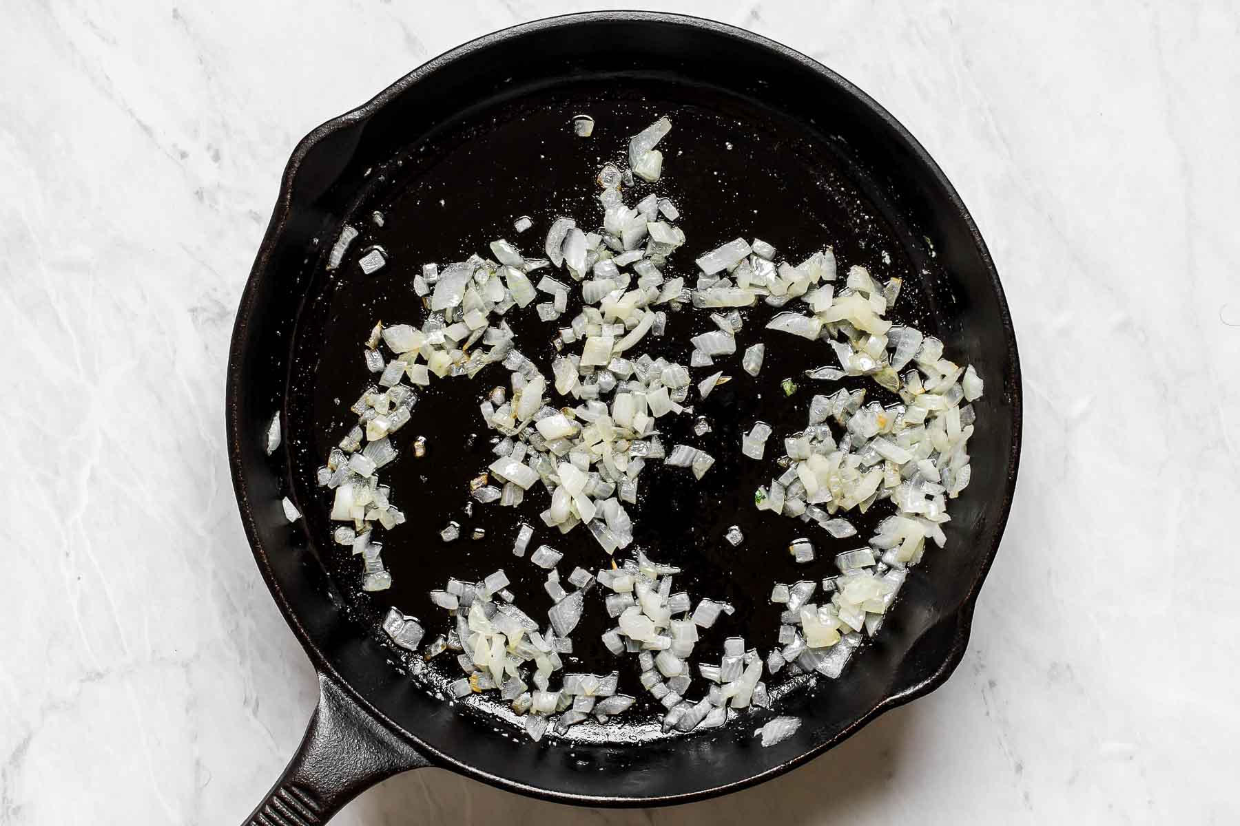 Onions sautéing in oil in a cast iron skillet.